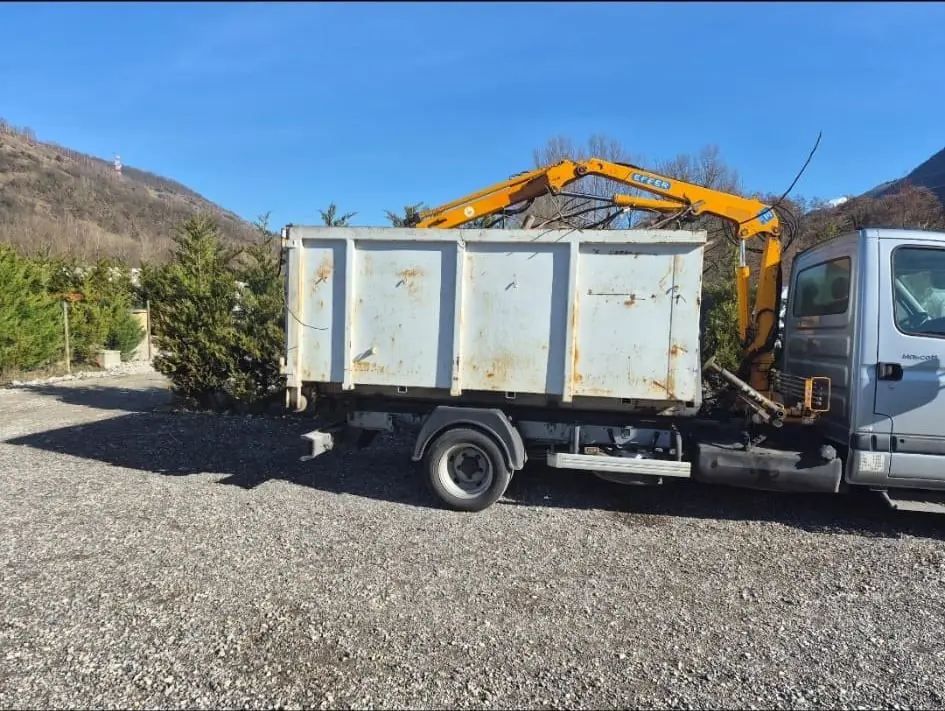 Le camion-benne de Perreau récupération, grue repliée, de profil sur un terrain gravillonné.