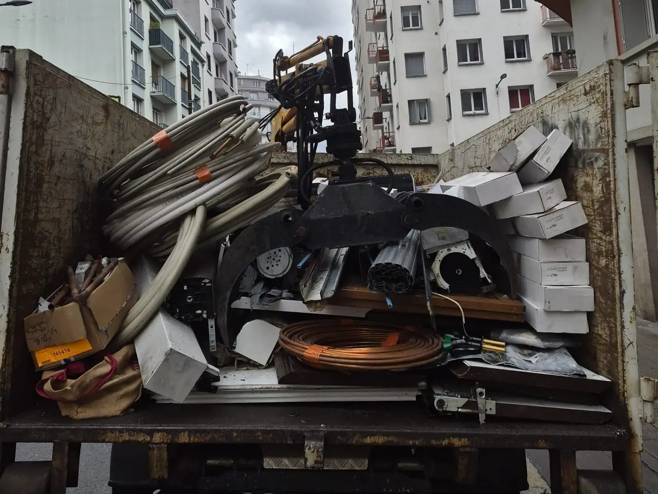 Couronnes de tubes de cuivre, câbles et pièces métalliques dans la benne du camion, garé dans une rue d’immeubles.
