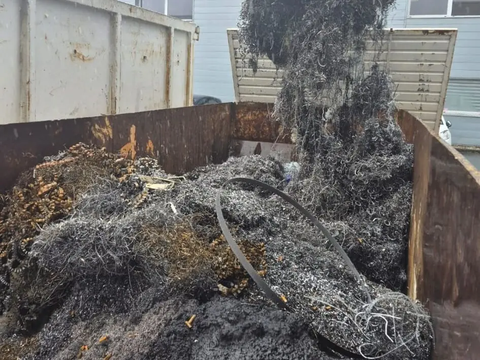 Le grappin de la grue déverse un amas de copeaux et de fils métalliques dans une benne.